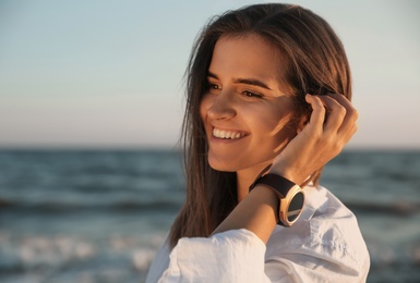 Photo of Young woman wearing smart watch on beach at sunset