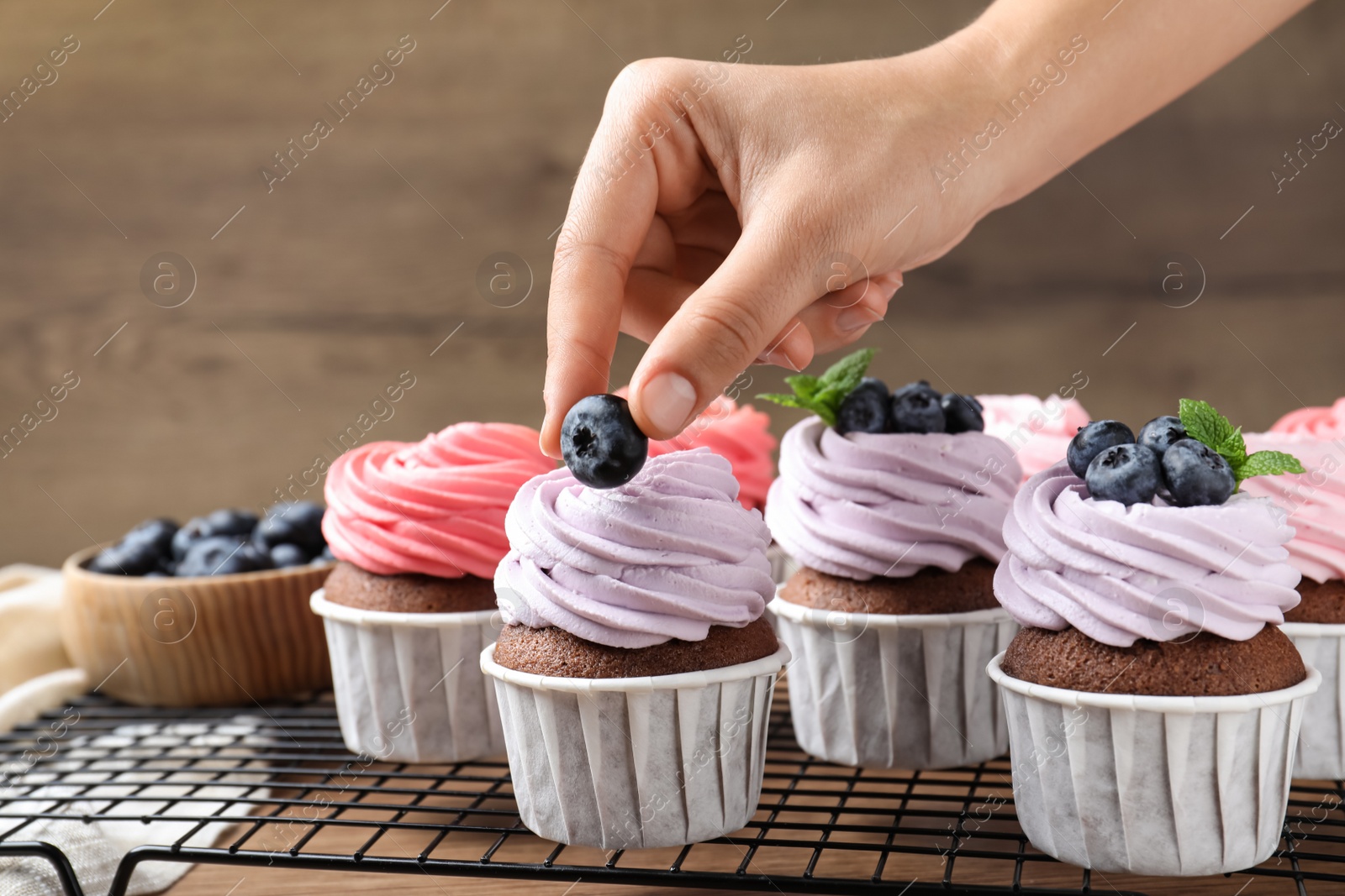 Photo of Woman decorating cupcake with fresh blueberry at wooden table, closeup