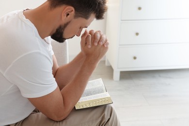 Photo of Religious man with Bible praying indoors. Space for text