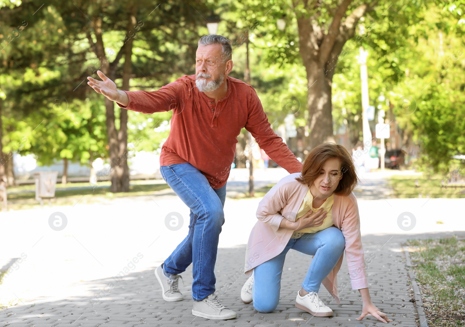 Photo of Man helping mature woman suffering from heart attack in park