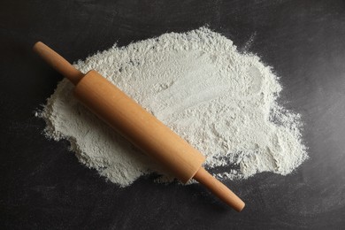 Flour and rolling pin on black table, top view