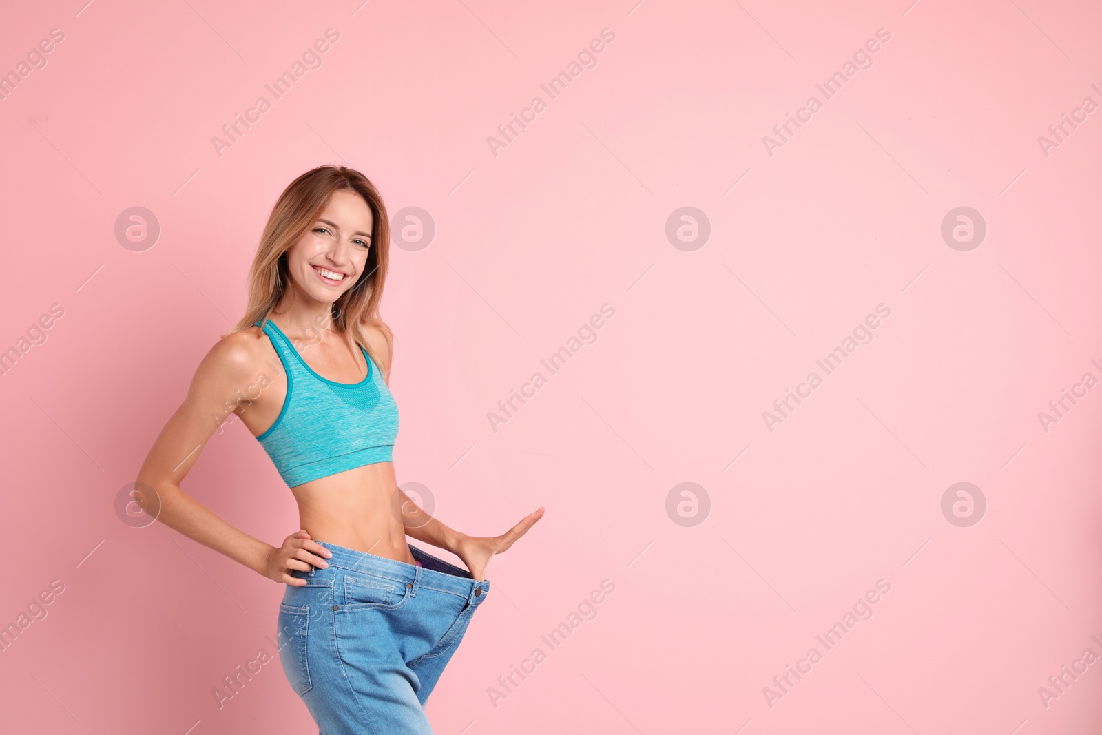 Photo of Young slim woman in old big jeans showing her diet results on color background