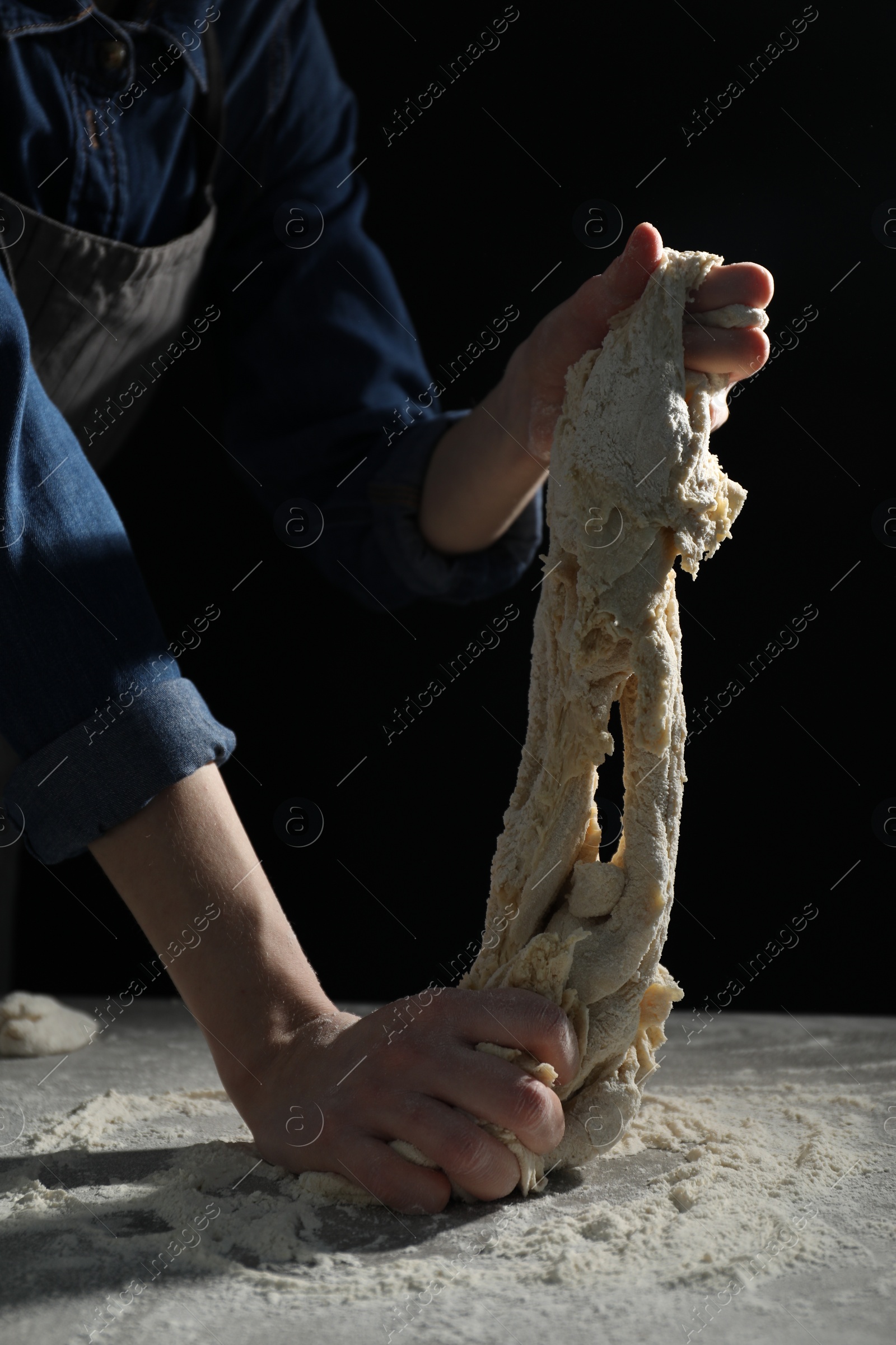 Photo of Making bread. Woman kneading dough at table on dark background, closeup