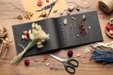 Photo of Flat lay composition with beautiful dry flowers and herbarium album on wooden table