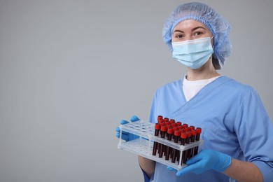 Laboratory testing. Doctor with blood samples in tubes on light grey background, space for text
