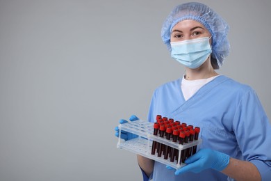 Photo of Laboratory testing. Doctor with blood samples in tubes on light grey background, space for text