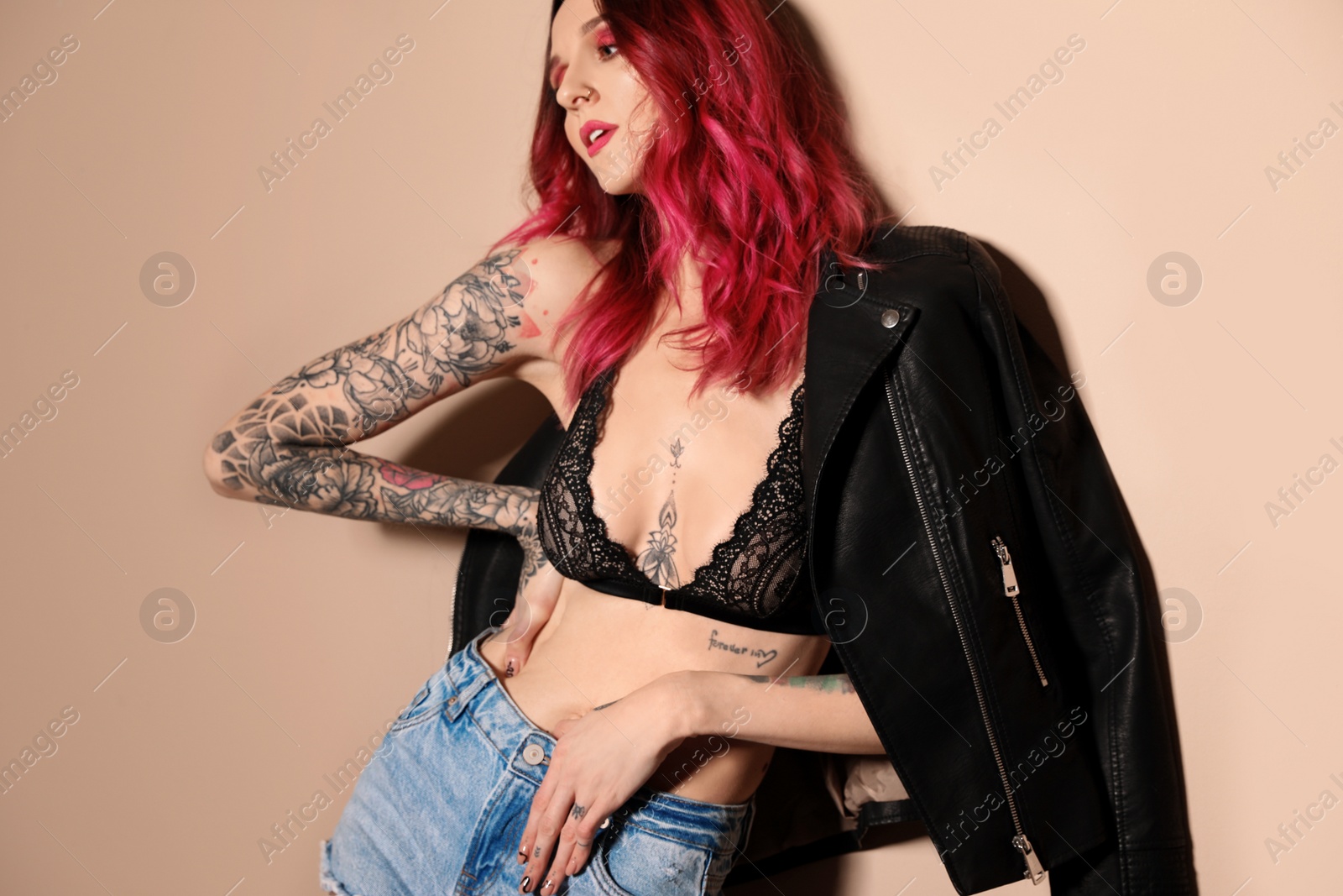 Photo of Beautiful woman with tattoos on body against beige background