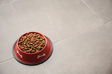 Photo of Dry dog food in feeding bowl on tiled floor. Space for text