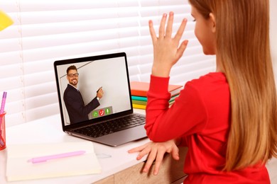 E-learning. Little girl raising her hand to answer during online lesson at table indoors