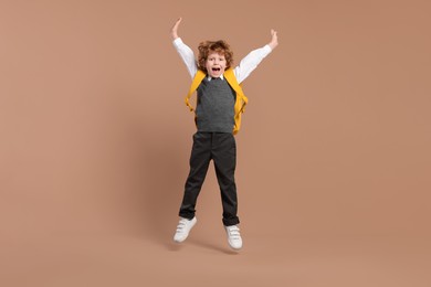 Happy schoolboy with backpack jumping on brown background
