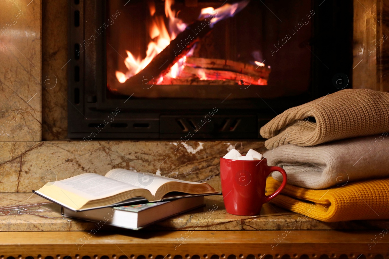 Photo of Stack of warm sweaters, cup, books and fireplace indoors
