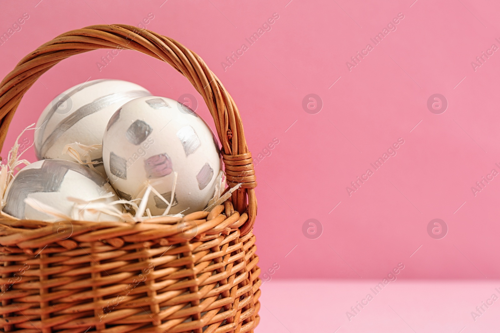 Photo of Basket of Easter eggs on table against color background, closeup. Space for text