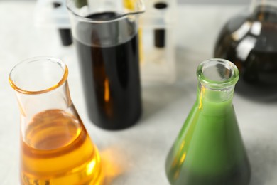 Photo of Laboratory glassware with different types of oil on white table, closeup