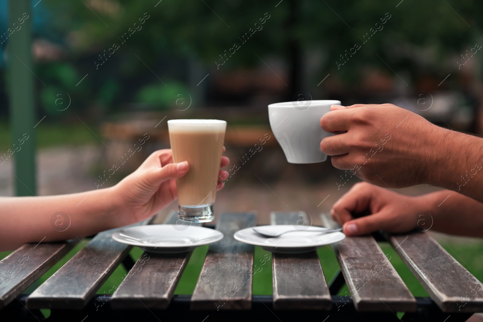 Photo of Man and woman drinking coffee at wooden table in outdoor cafe, closeup