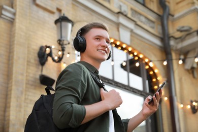 Photo of Smiling man in headphones and smartphone outdoors, low angle view