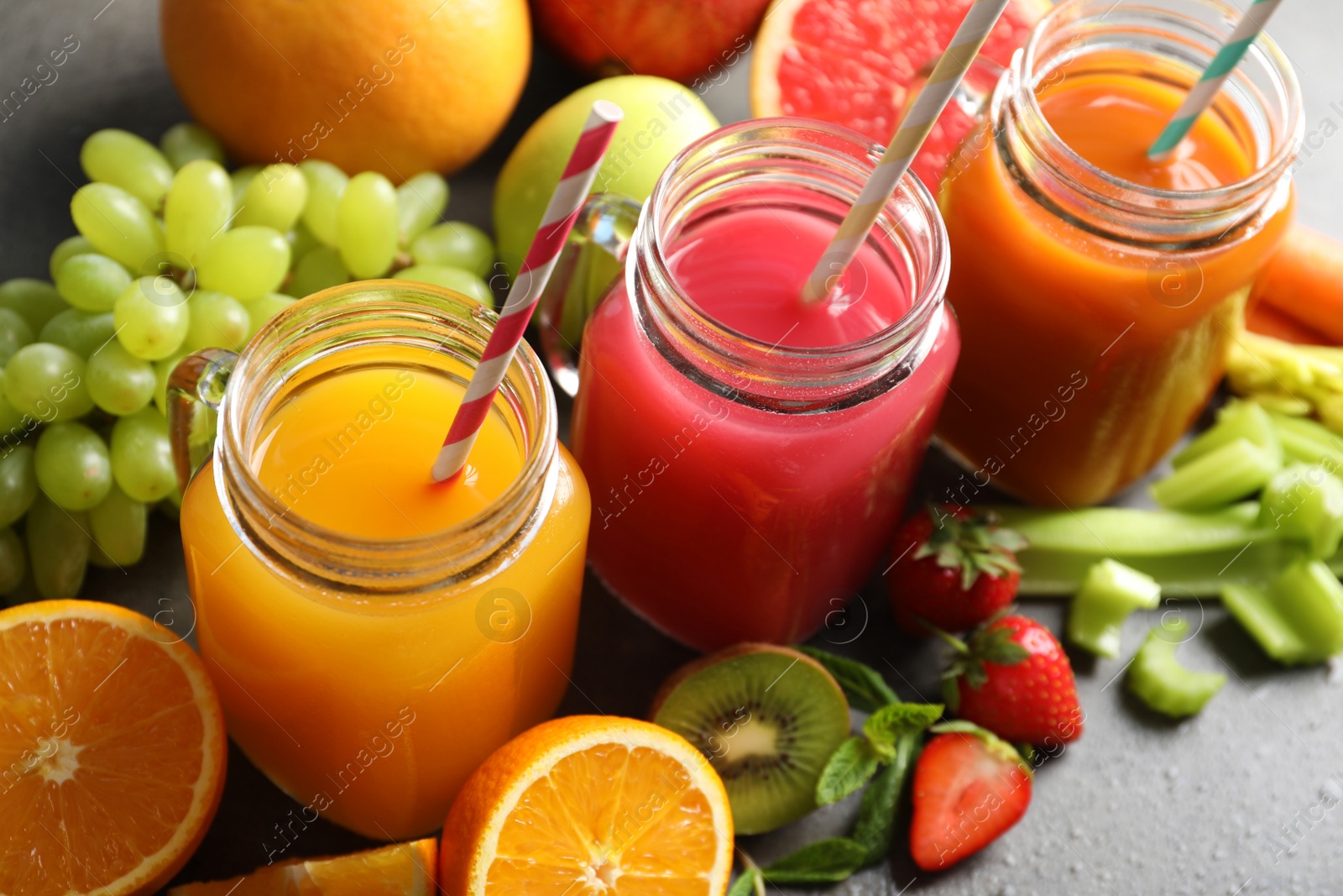 Photo of Different juices in mason jars and fresh ingredients on grey table