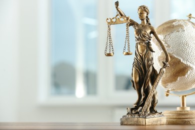 Photo of Figure of Lady Justice and globe on table indoors, space for text. Symbol of fair treatment under law
