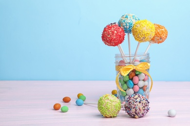 Photo of Glass jar with tasty cake pops and dragee on table against light blue background, space for text