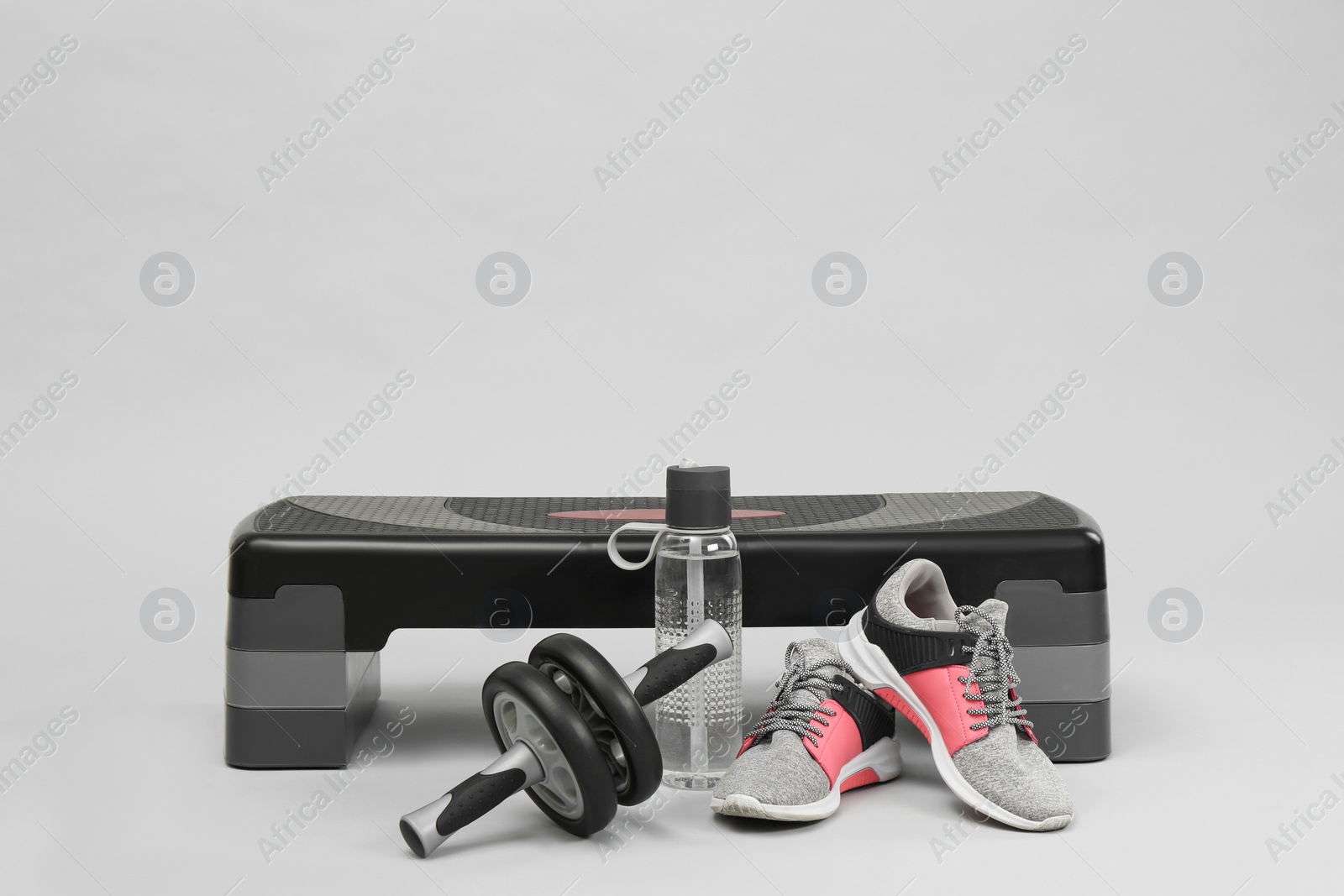 Photo of Step platform, abdominal wheel, water bottle and sneakers on light background, space for text. Sport equipment