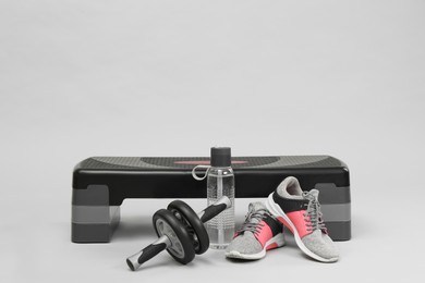 Photo of Step platform, abdominal wheel, water bottle and sneakers on light background, space for text. Sport equipment