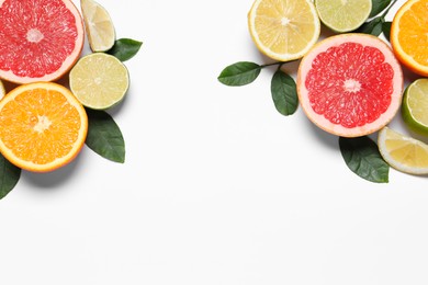 Photo of Different cut citrus fruits and leaves on white table, flat lay. Space for text