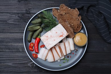 Photo of Pork fatback with spices, rye bread and pickled cucumbers on black wooden table, flat lay