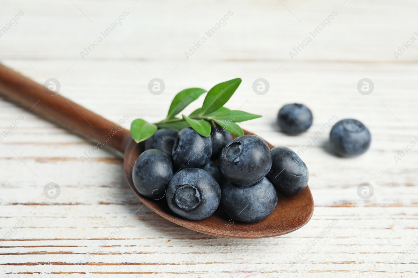 Photo of Wooden spoon of fresh blueberries with leaves on white table