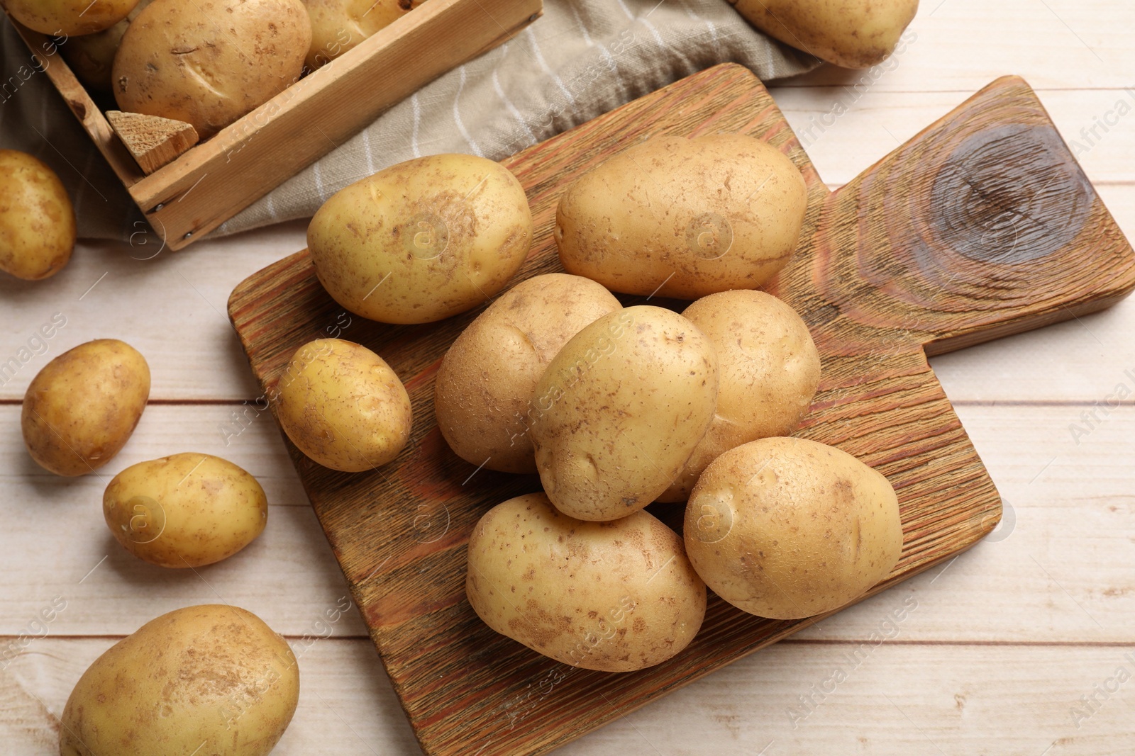 Photo of Raw fresh potatoes and cutting board on light wooden table, top view