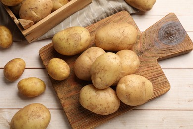 Photo of Raw fresh potatoes and cutting board on light wooden table, top view