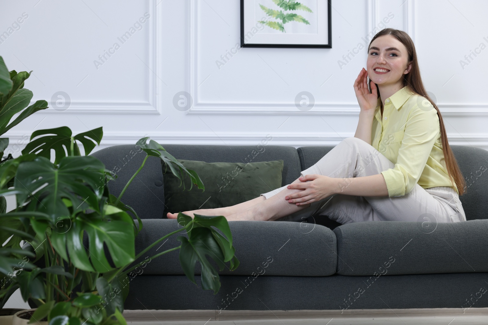 Photo of Beautiful young woman on sofa in room with green houseplants