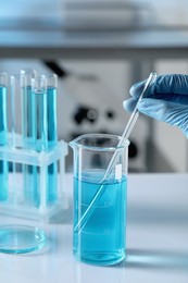 Photo of Scientist taking sample of light blue liquid in laboratory, closeup