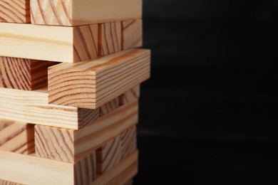 Photo of Jenga tower made of wooden blocks on black background, closeup. Space for text