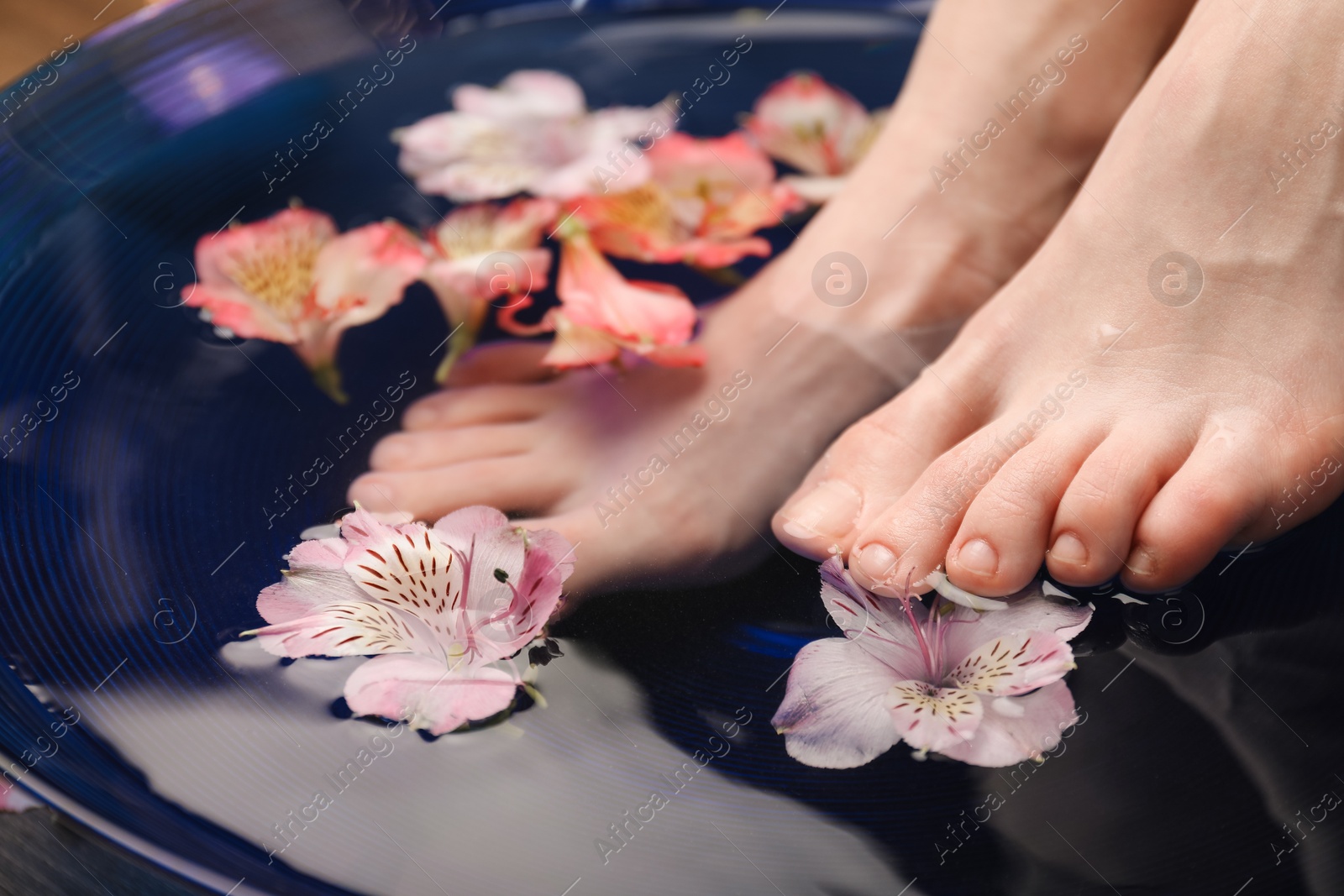 Photo of Woman soaking her feet in bowl with water and flowers, closeup. Spa treatment