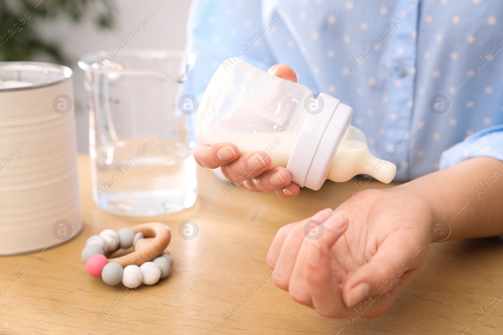 Photo of Woman checking temperature of infant formula at table, closeup. Baby milk