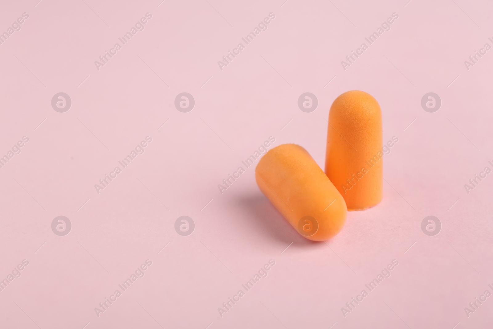 Photo of Pair of orange ear plugs on pink background. Space for text