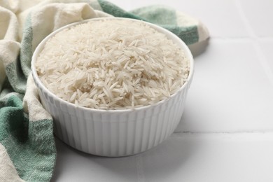 Photo of Raw basmati rice in bowl on white tiled table, closeup