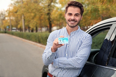 Photo of Young man holding driving license near open car. Space for text