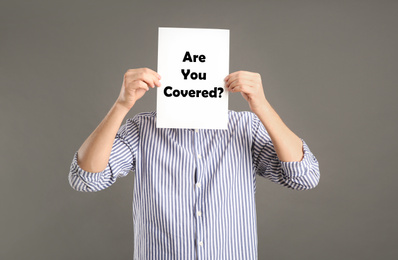 Image of Man holding paper with text ARE YOU COVERED? on grey background. Insurance concept