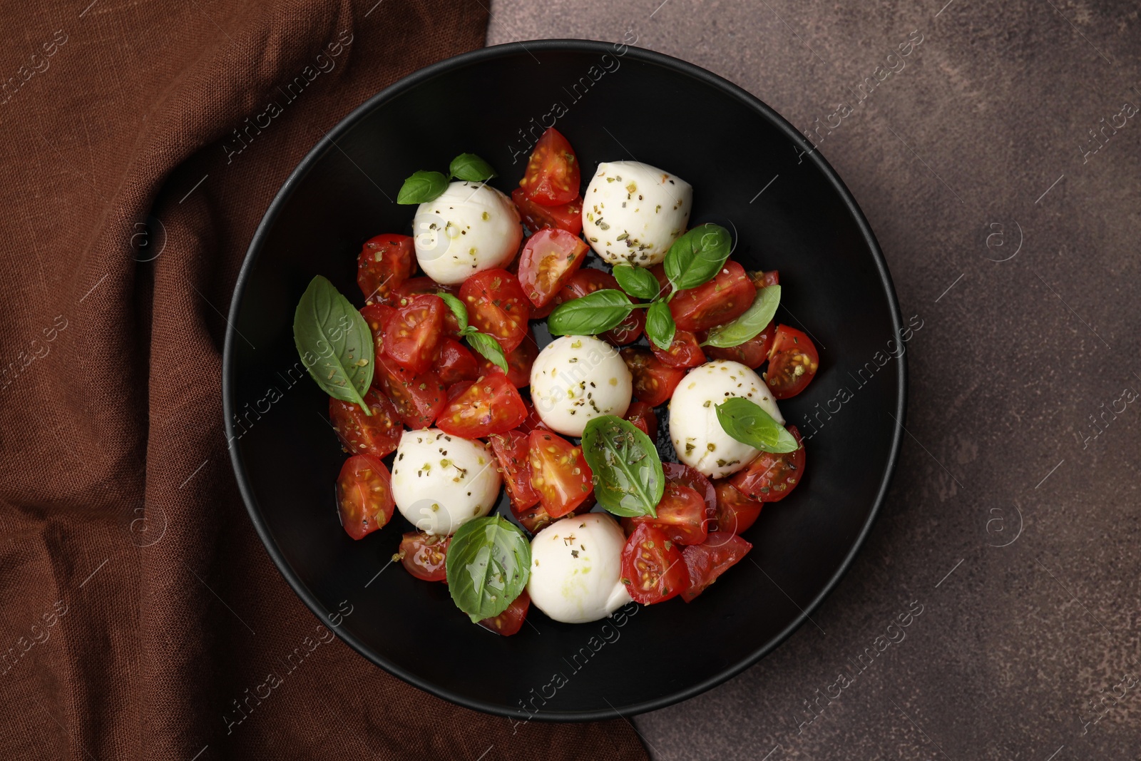 Photo of Tasty salad Caprese with tomatoes, mozzarella balls and basil on brown table, top view