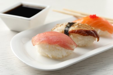 Plate with delicious nigiri sushi and soy sauce on white wooden table, closeup