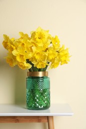 Photo of Beautiful daffodils in vase on white table near light wall
