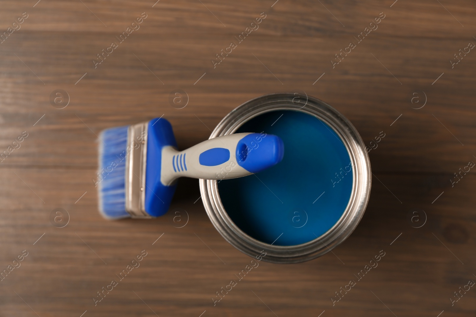 Photo of Can of blue paint and brush on wooden background, top view