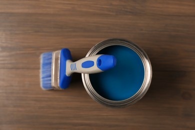 Photo of Can of blue paint and brush on wooden background, top view