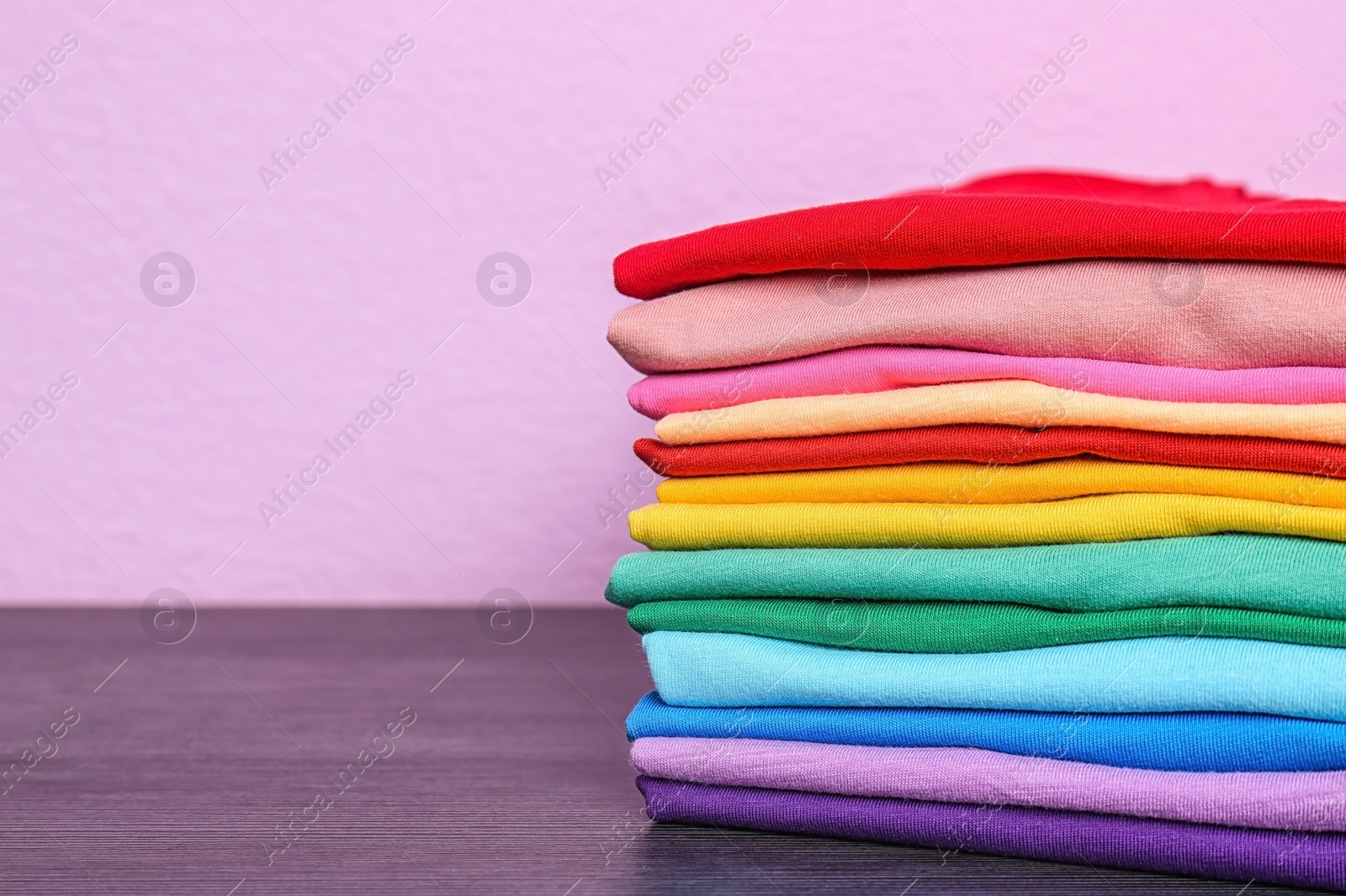 Photo of Stack of colorful t-shirts on table against color background