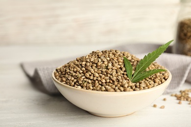 Photo of Bowl of hemp seeds on table against wooden wall