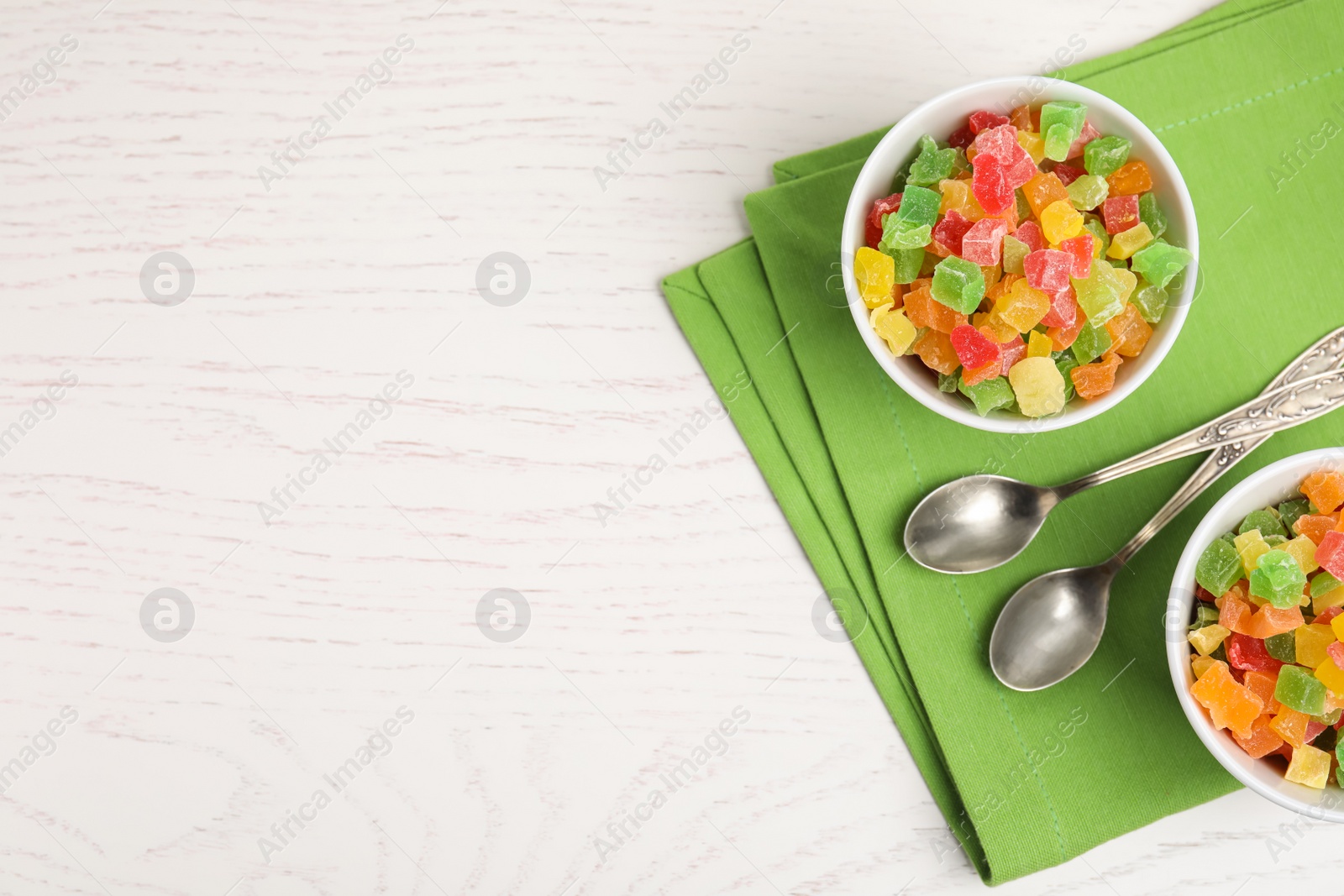 Photo of Spoons and bowls with delicious candied fruits on white wooden table, flat lay. Space for text