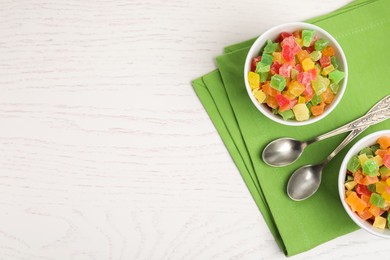 Spoons and bowls with delicious candied fruits on white wooden table, flat lay. Space for text