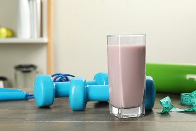 Photo of Tasty shake, sports equipment and measuring tape on wooden table indoors. Weight loss