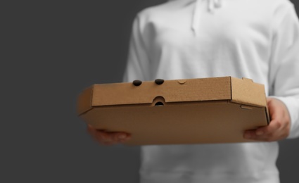 Photo of Young woman with pizza box on grey background, closeup. Food delivery service