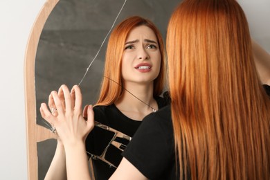 Mental problems. Disappointed young woman looking at herself in broken mirror indoors